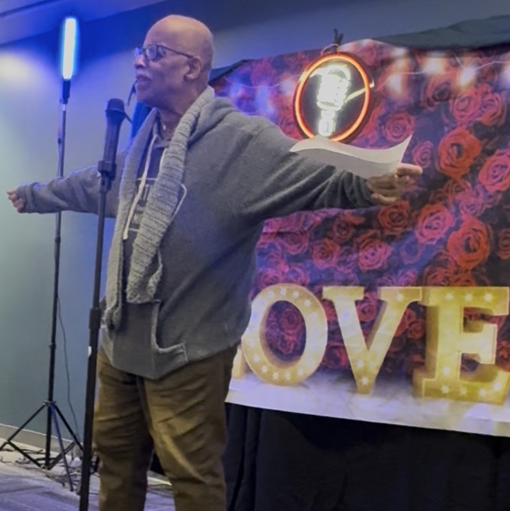 Poet performing on stage under warm amber spotlight, expressive gesture, intimate venue, dark atmospheric background